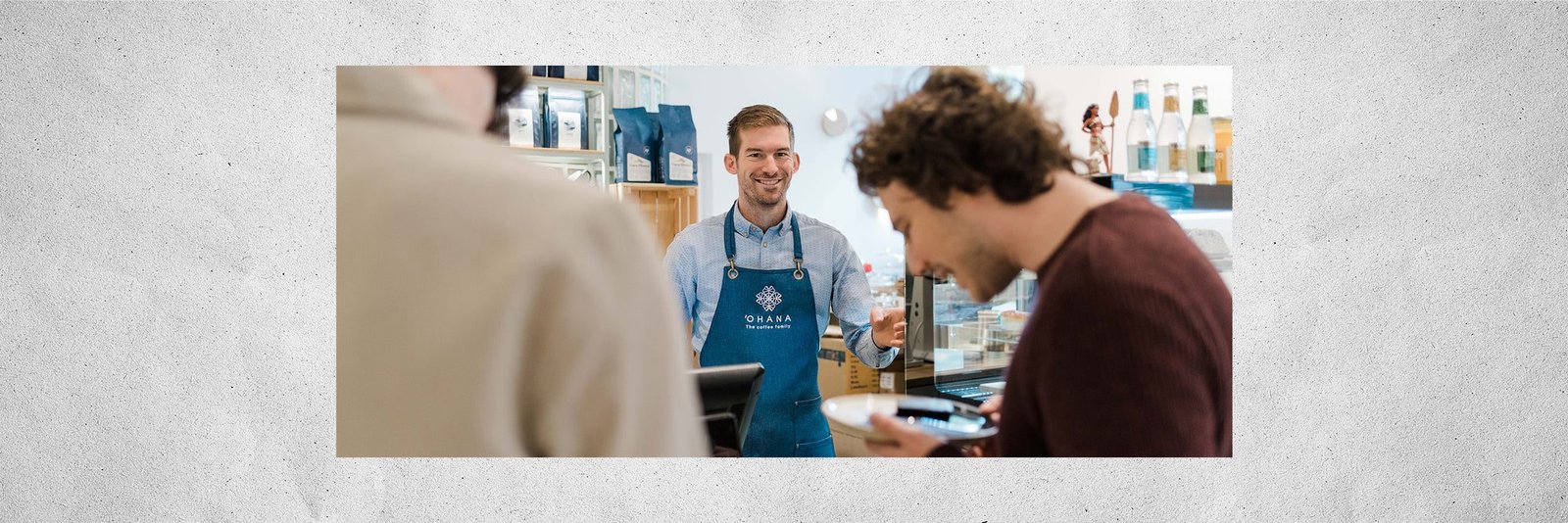Mosolygó ‘Ohana barista kék kötényben fogadja a vendégeket a pultnál